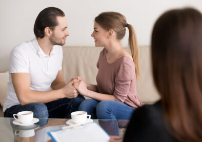 Excited loving couple sitting on sofa holding hands looking in the eyes, meeting with wedding planner, choosing place for honeymoon trip, successful marriage therapy with family psychologist